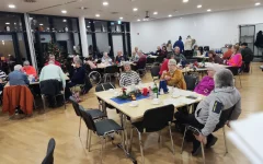 Der Saal füllt sich. An den Tischen sitzen einige Besucher*innen.