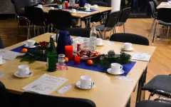 Nahaufnahme der Tischdekoration: Auf dem Tisch liegt ein dunkelblauer Tischläufer, darauf sind Tannenzweige, rote Kerzen, Keksteller und Tannenzapfen drappiert. 