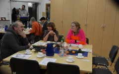 Besucher*innen der Adventsfeier unterhalten und lachen gemeinsam an den Tischen sitzend. 