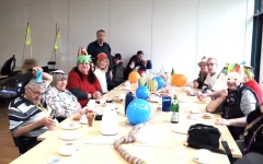 Die Teilnehmer des Dienstagstreff sitzen in feierlicher Stimmung am geschmückten Tisch. Die meisten von ihnen tragen ihre selbstgebastelten Masken.