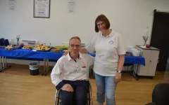  Ralf Bockstedte (Vorsitzender des Inklusionsbeirats) im Rollstuhl und Angela Ströter stehend vor dem Kuchenbuffet 