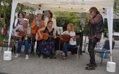  Der Musikkreis in Aktion unter einem weißen Pavillon. Darunter drei Gitarrenspieler/innen, ein Mundharmonika-Spieler und drei Sängerinnen 