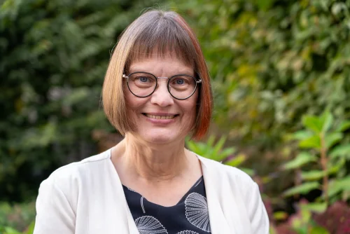 Angela Ströter lächelt in die Kamera. Sie trägt eine Brille, einen weißen Blazer mit einem dunklen&nbsp;Oberteil.&nbsp;