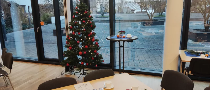 Der Georg-Gottlob-Saal ist feierlich geschmückt. Am Fenster zum Hof steht ein Weihnachtsbaum, der mit roten Kugeln geschmückt ist. Im Vordergrund ist ein dekorierter Tisch.