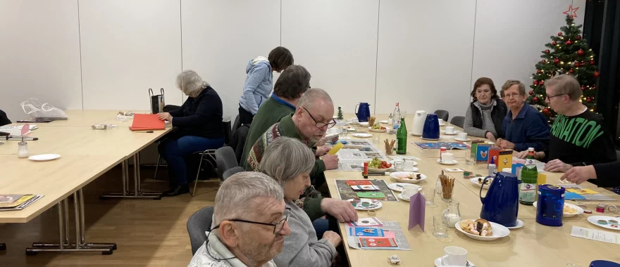 Die Dienstagstreffler*innen sitzen gemeinsam am Tisch und basteln, essen Kuchen und trinken Kaffee. 